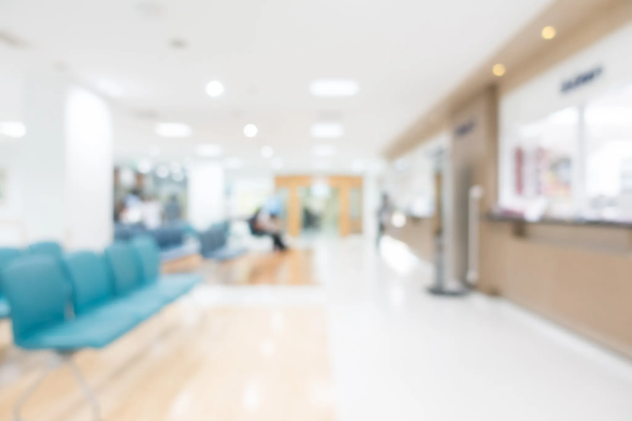 Sala d’attesa di ospedale sfocata con sedie azzurre e reception